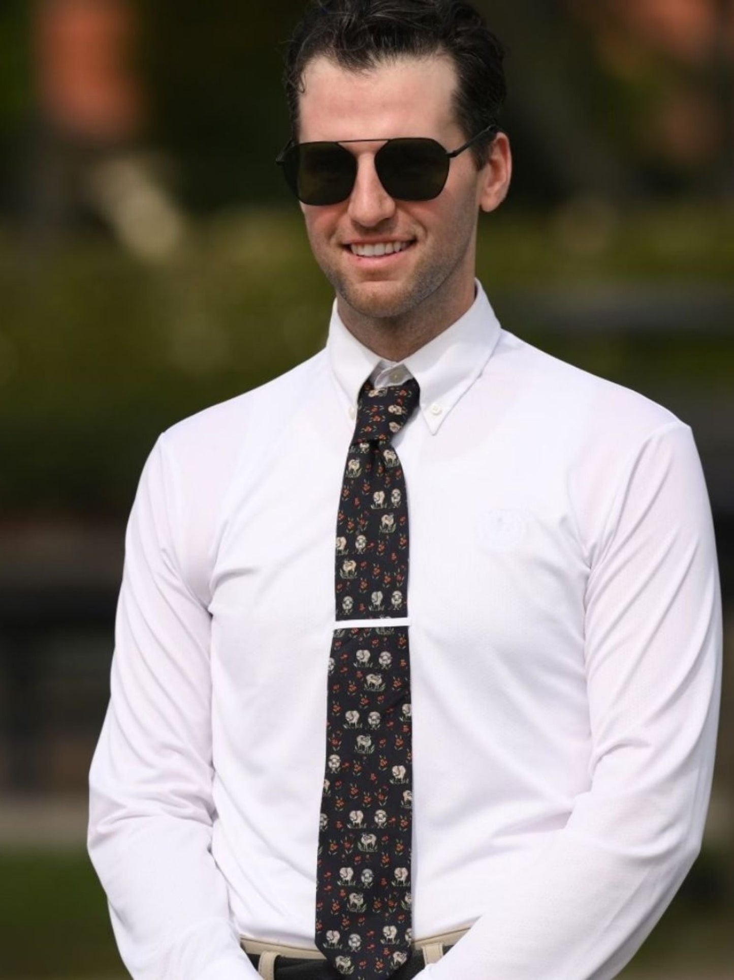 Man wearing a white shirt and patterned tie with sunglasses, outdoors.