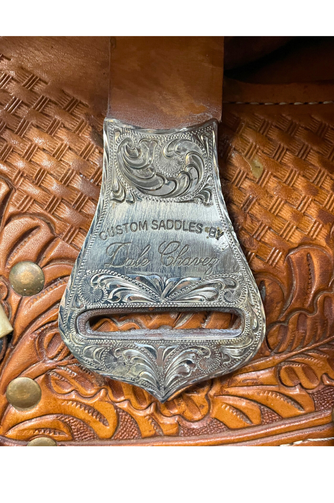 Silver saddle buckle on a leather background with 'Custom Saddles' branding.
