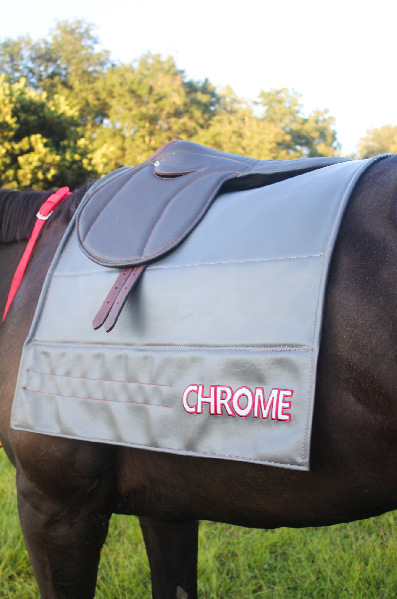 A gray custom embroidered saddle pad with pink embroidery on the sides.