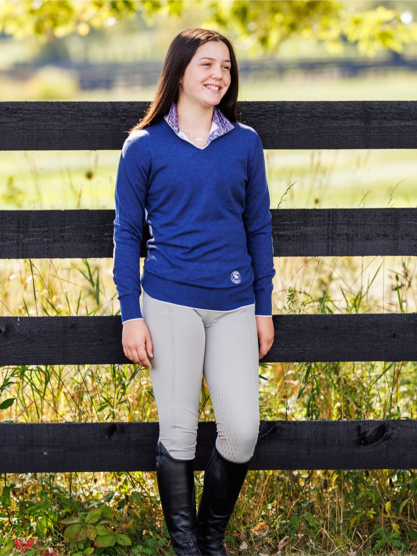 Woman in equestrian attire standing next to a wooden fence in a field