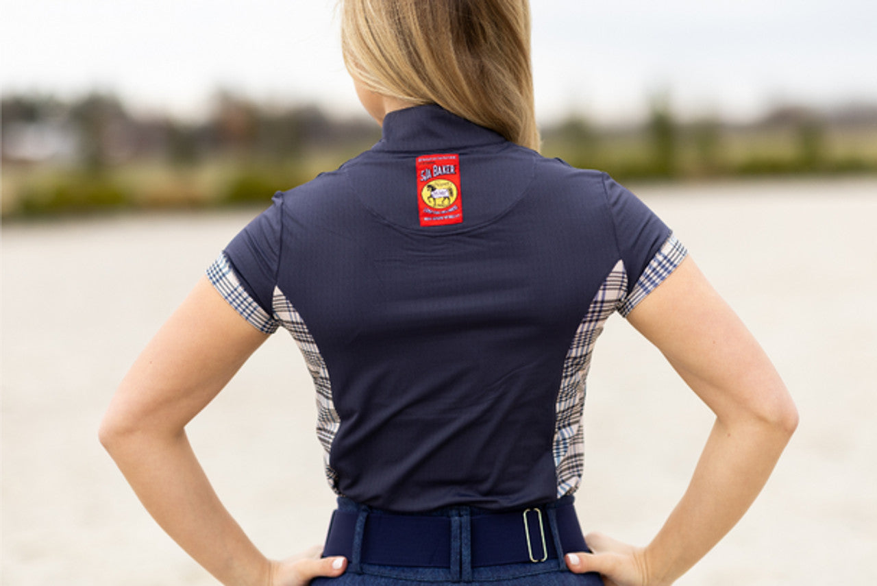 Person wearing a navy polo shirt with a logo on the back, standing outdoors by a body of water.