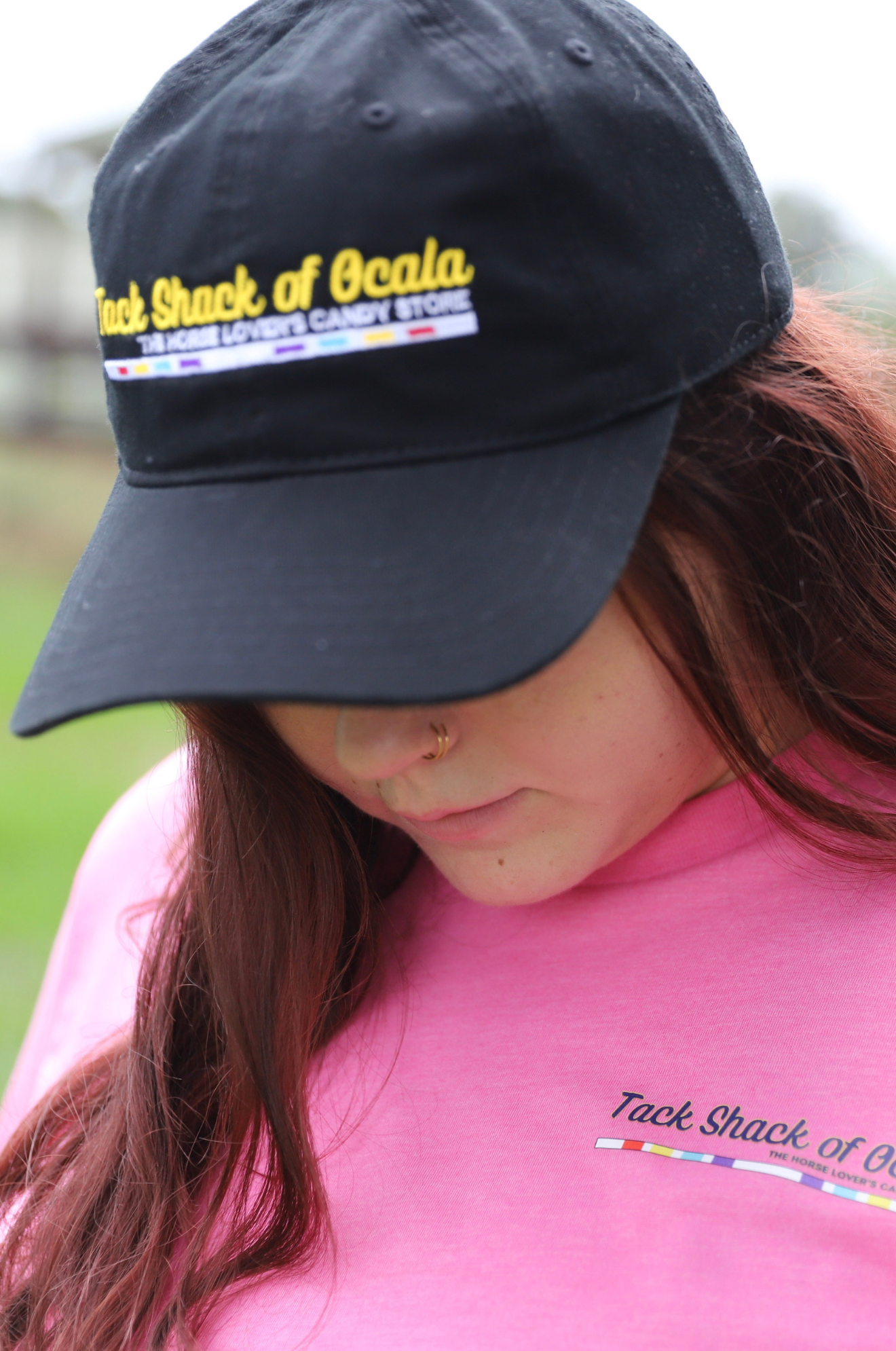 Person wearing a black cap and pink shirt with 'Tack Shack of Ocala' branding.