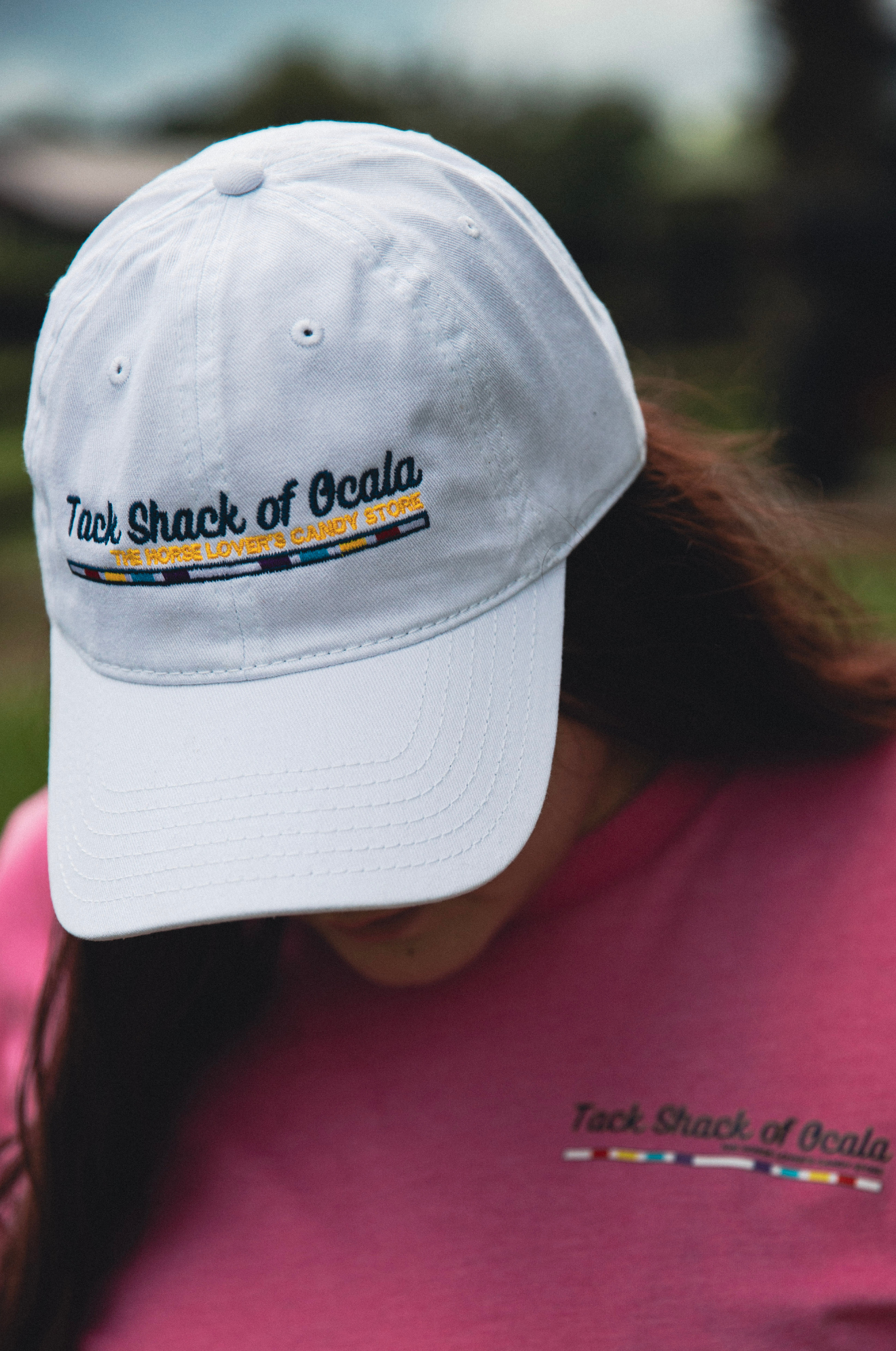 Person wearing a white cap with 'Tack Shack of Ocala' logo, blurred background