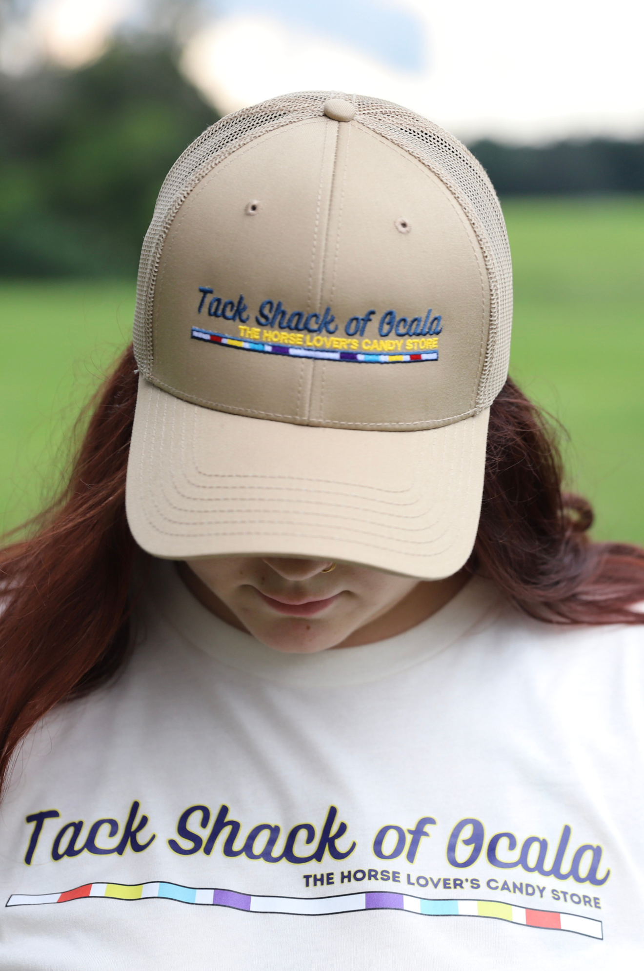 Person wearing a beige cap and white shirt with 'Tack Shack of Ocala' branding outdoors.