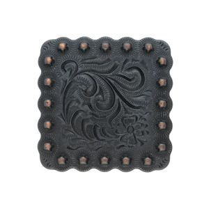 A square black metal decorative piece with a scalloped edge, featuring an embossed floral and scroll pattern in the center and a border of raised studs, shown on a plain white background.
