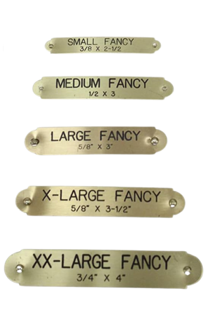 A variety of brass fancy plates in different sizes, arranged in a line, with visible engraved text indicating different sizes such as 'SMALL FANCY', 'MEDIUM FANCY', 'LARGE FANCY', 'X-LARGE FANCY', and 'XX-LARGE FANCY'.