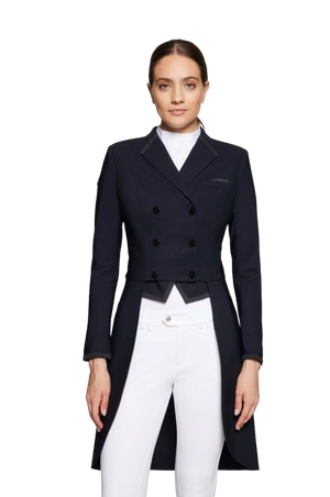 A woman standing, wearing a navy blue tuxedo with a mandarin collar, black lapels, and a front lined with silver buttons. She has a white shirt and is wearing riding pants.