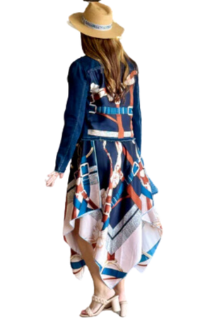 A woman viewed from the back wearing a multicolored scarf dress with a geometric pattern, paired with a denim jacket and a wide-brimmed hat.