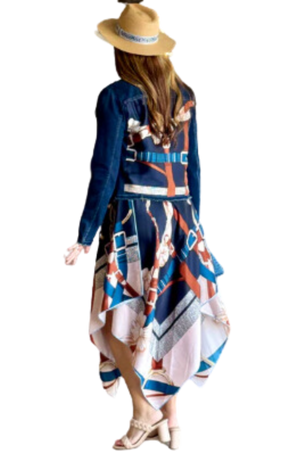 A woman viewed from the back wearing a multicolored scarf dress with a geometric pattern, paired with a denim jacket and a wide-brimmed hat.