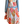 A woman viewed from the back wearing a multicolored scarf dress with a geometric pattern, paired with a denim jacket and a wide-brimmed hat.