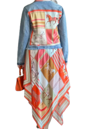 A woman viewed from the back wearing a multicolored scarf dress with a geometric pattern, paired with a denim jacket and a wide-brimmed hat.