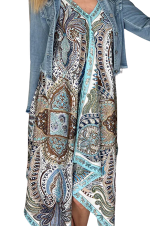 A woman viewed from the back wearing a multicolored scarf dress with a geometric pattern, paired with a denim jacket and a wide-brimmed hat.