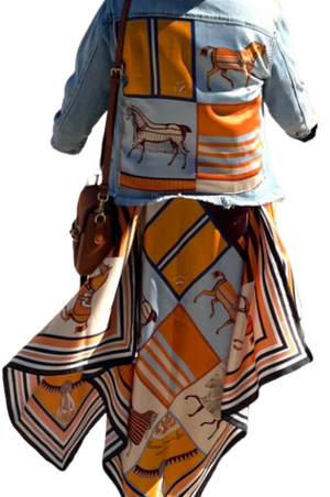 A woman viewed from the back wearing a multicolored scarf dress with a geometric pattern, paired with a denim jacket and a wide-brimmed hat.