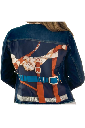 The image displays the back view of a blue denim jacket with a decorative pattern featuring gold and white elements.