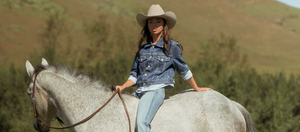 Woman in a cowboy hat riding a horse with a scenic background