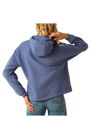 A female model wearing a maroon hoodie with a logo on the front, paired with blue denim shorts and a matching maroon cap.