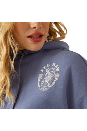 A female model wearing a maroon hoodie with a logo on the front, paired with blue denim shorts and a matching maroon cap.