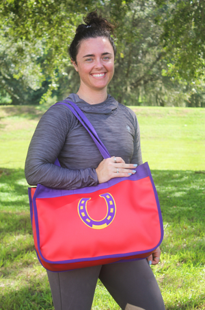 A red and blue paddock bag with a large yellow horseshoe logo on the front and purple straps.