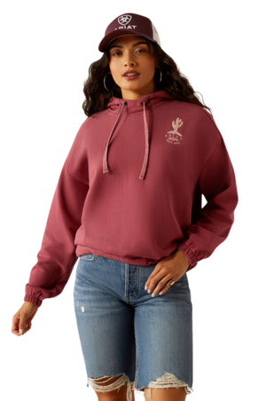 A female model wearing a maroon hoodie with a logo on the front, paired with blue denim shorts and a matching maroon cap.