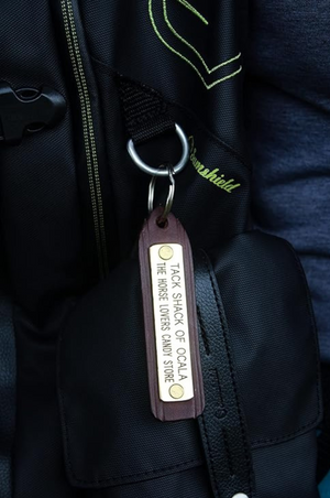 A custom leather key chain with a brass engraved plate, showing the store name and logo.