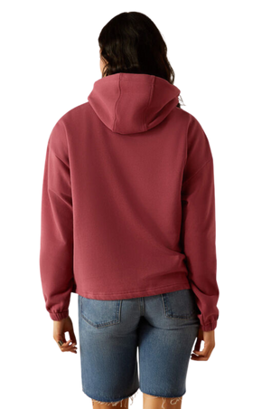 A female model wearing a maroon hoodie with a logo on the front, paired with blue denim shorts and a matching maroon cap.