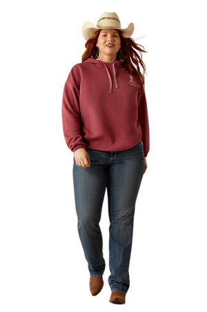 A female model wearing a maroon hoodie with a logo on the front, paired with blue denim shorts and a matching maroon cap.