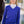 Woman wearing a blue sweater with a white shirt underneath, standing next to a horse.