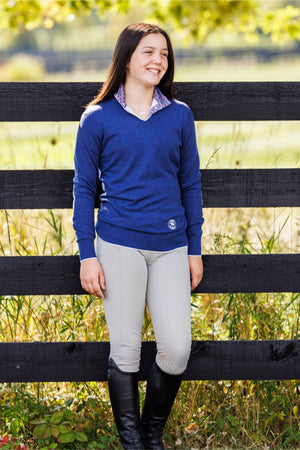 Woman in equestrian attire standing next to a wooden fence in a field