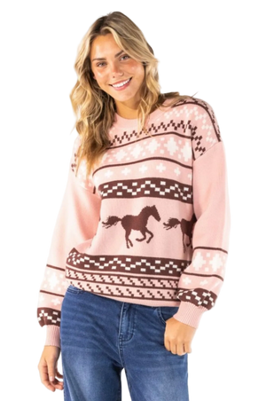 A woman wearing a pink and brown knit sweater with a horse design, paired with blue jeans, against a plain white background.