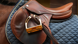 Brown leather saddle with gold stirrup on a blue quilted pad.