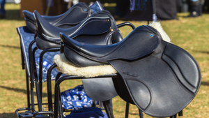 Row of black equestrian saddles on stands outdoors