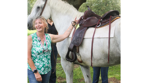 Woman standing next to a white horse with a saddle, outdoors.
