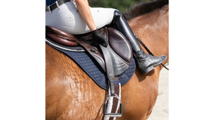 Close-up of a horse saddle with a rider's foot in a stirrup, on a plain background