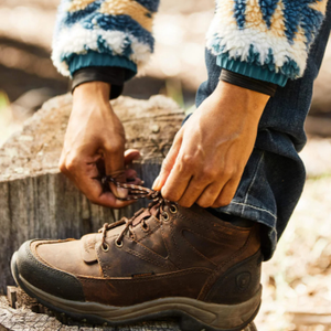 Person tying a brown hiking boot with a blurred natural background