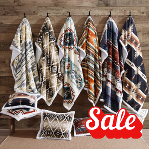 Set of patterned throws and a pillow on hooks with a 'Sale' sign against a wooden wall.