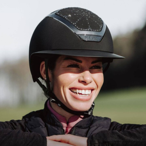 Person wearing a black riding helmet with a blurred outdoor background