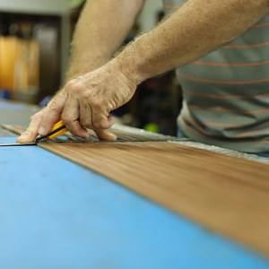 Person cutting a piece of wood with a ruler on a blue surface