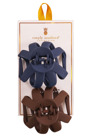 Two hair clips, one green and one brown, displayed on a vertical cardboard stand with a logo at the top.