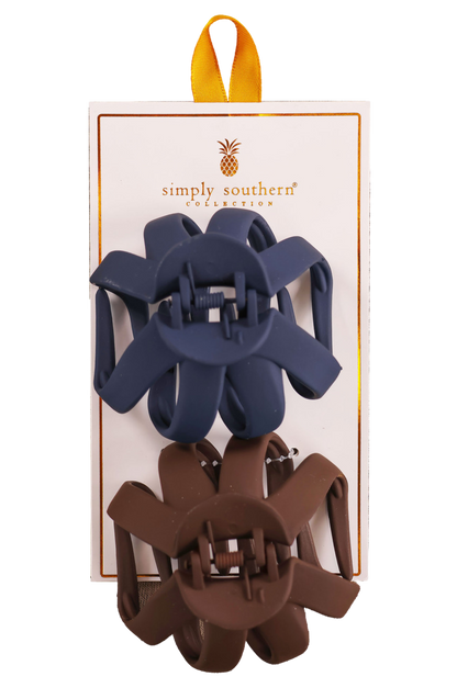 Two hair clips, one green and one brown, displayed on a vertical cardboard stand with a logo at the top.