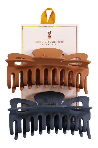 Two hair clips, one green and one brown, displayed on a vertical cardboard stand with a logo at the top.