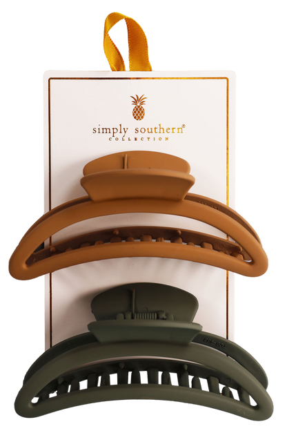 Two hair clips, one green and one brown, displayed on a vertical cardboard stand with a logo at the top.