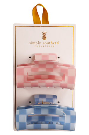 Two hair clips, one green and one brown, displayed on a vertical cardboard stand with a logo at the top.