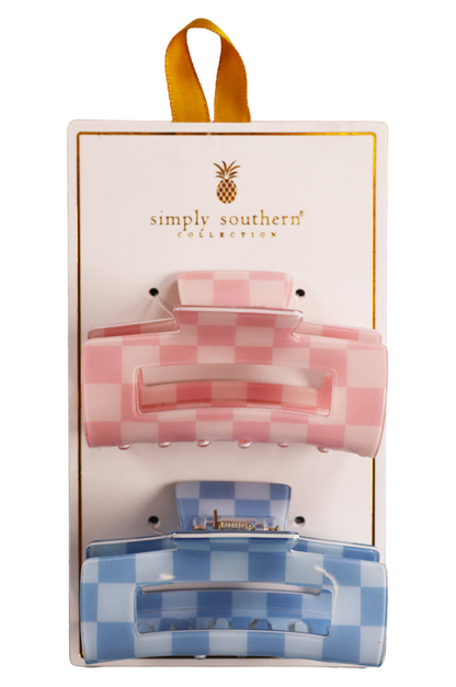 Two hair clips, one green and one brown, displayed on a vertical cardboard stand with a logo at the top.