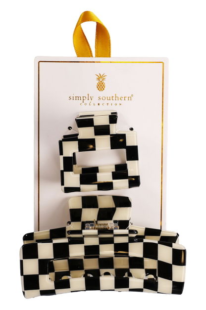 Two hair clips, one green and one brown, displayed on a vertical cardboard stand with a logo at the top.