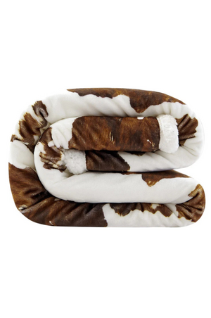 A sherpa throw with a cowhide print pattern in beige, brown, and white colors.