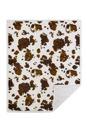 A sherpa throw with a cowhide print pattern in beige, brown, and white colors.