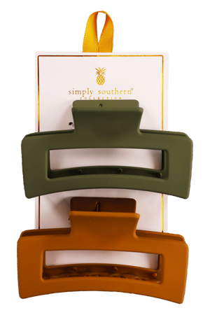 Two hair clips, one green and one brown, displayed on a vertical cardboard stand with a logo at the top.