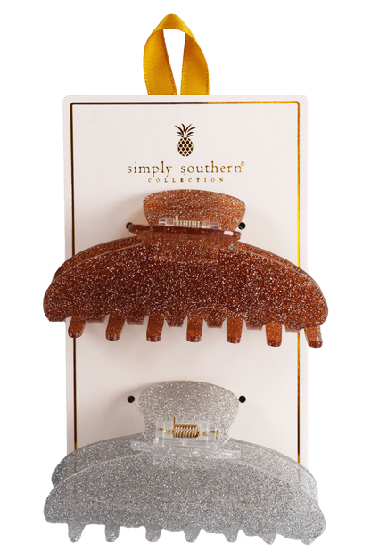 Two hair clips, one green and one brown, displayed on a vertical cardboard stand with a logo at the top.