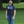 Person wearing a blue t-shirt with text and graphics, standing in a grassy area with trees.