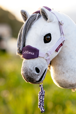 White horse wearing a purple bridle with 'LeMieux' branding, standing in a grassy field.